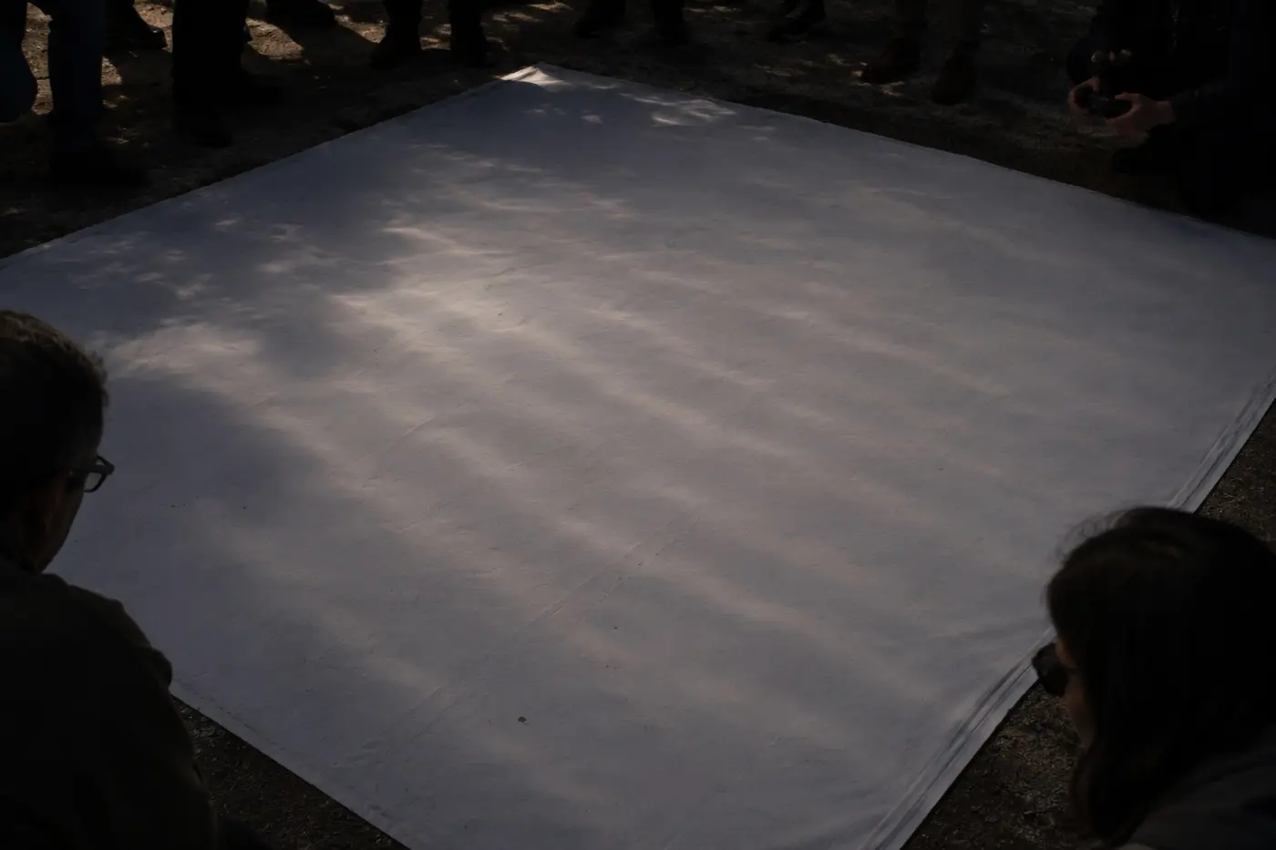 Um lençol branco estendido no chão para observar as bandas de sombra, rodeado de observadores.